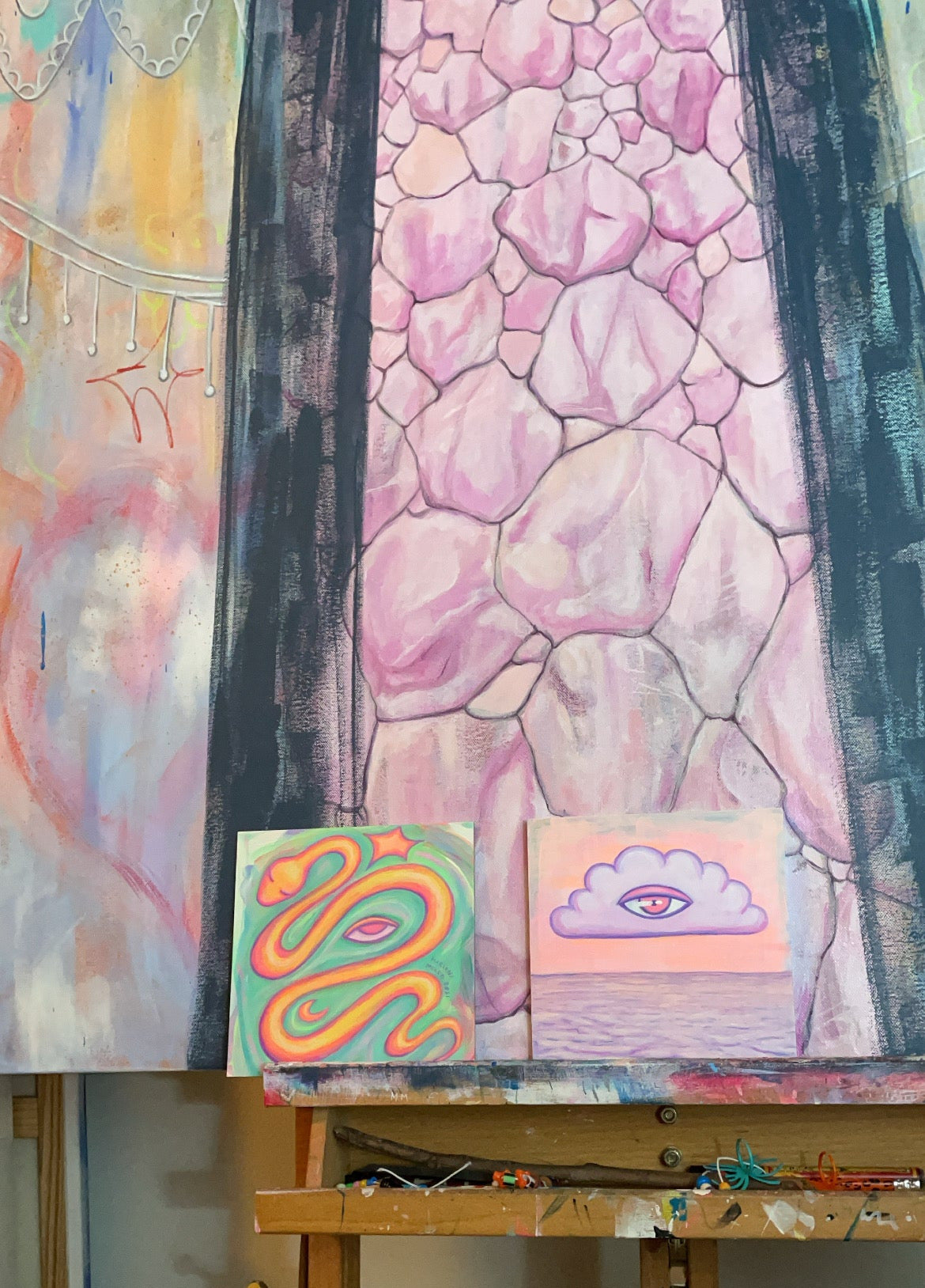 Colorful art pieces on an easel against a textured wall.